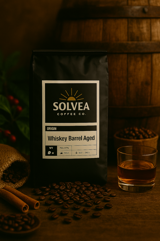 Solvea Coffee Co. Whiskey Barrel Aged coffee bag with coffee beans, glass of whiskey, and barrel in the background.